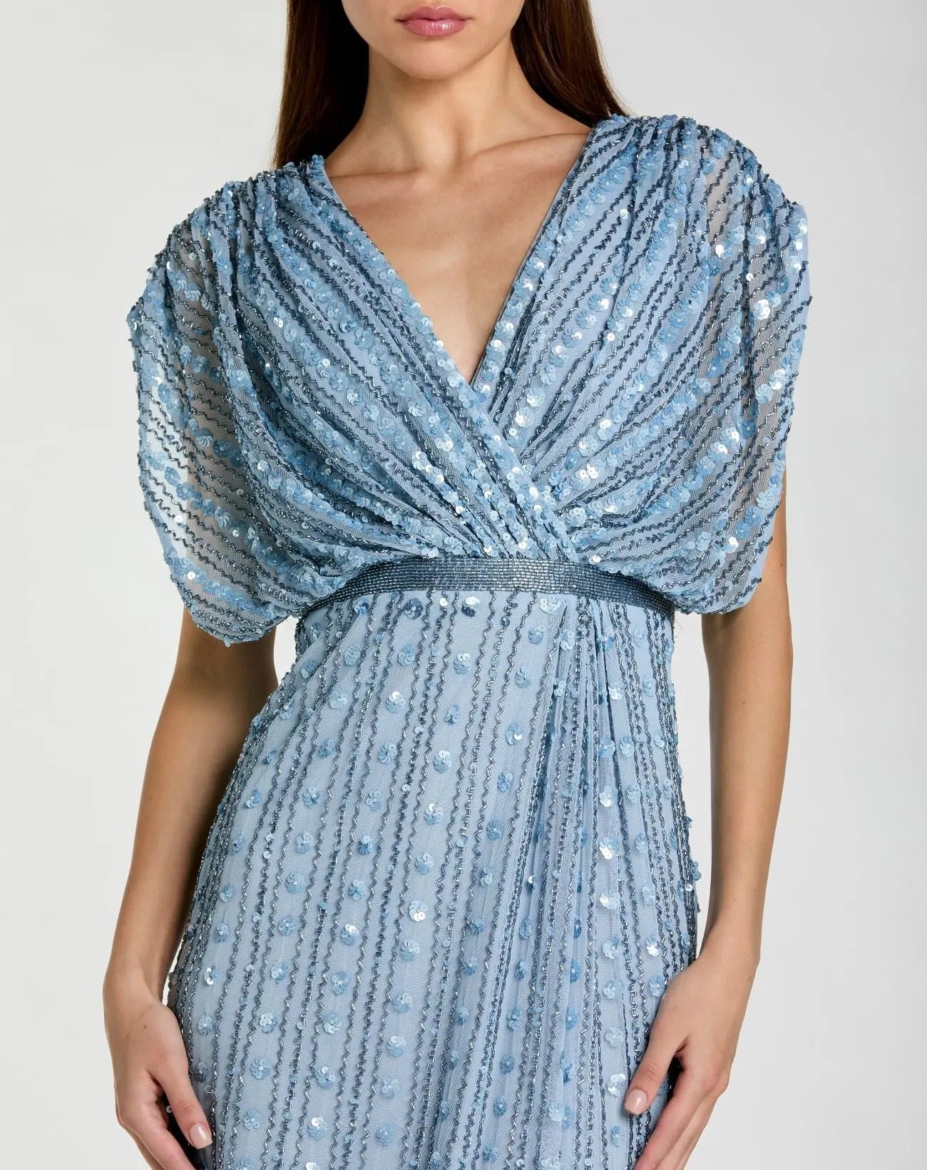 Woman wearing the Mac Duggal 23081 long formal dress in light blue, featuring sequin beading, short puff sleeves, and a deep V-neckline; shown from shoulders to mid-thigh.